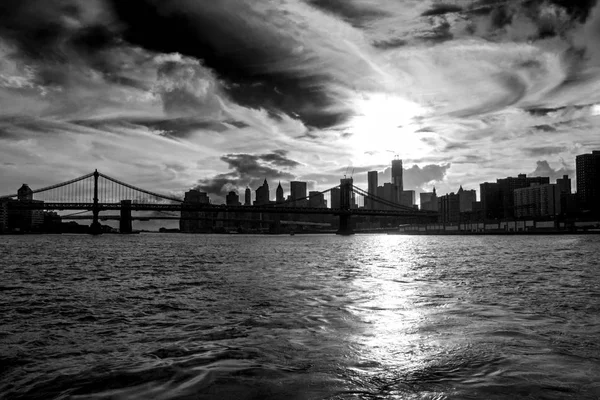 有名なマンハッタンとブルックリン橋 バック グラウンドでマンハッタンのダウンタウンの金融街とニューヨーク市 アメリカ合衆国 イースト川と美しい夕日の反射 黒と白の写真 — ストック写真
