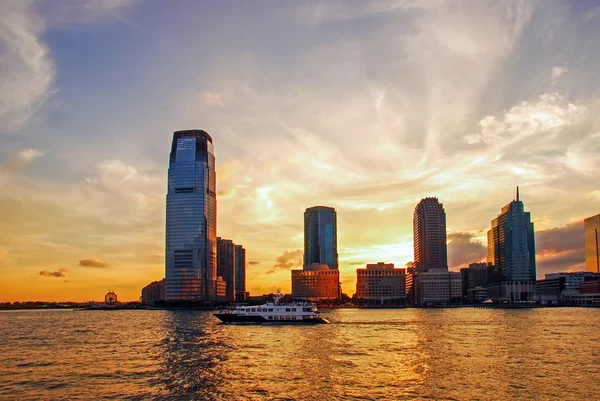 Jersey City shore with office buildings and the boat at night against the fantastic sunset sky in Jersey City, New Jersey, USA