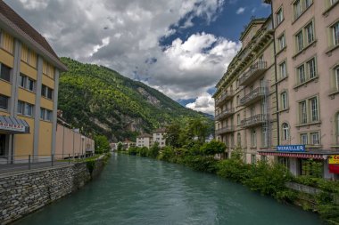 Interlaken, İsviçre - 19 Haziran 2015: Dramatik bulutlu gökyüzünün altında Aare Nehri 'nin turkuaz suyu, binalar ve İsviçre Alpleri ile geniş açı görüşü