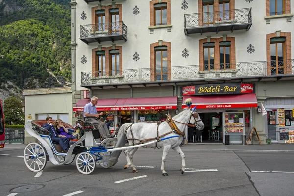 スイスインターラーケン2015年6月19日 スイスアルプスを背景に白い馬と店のある古典的な建物によって描かれた馬車に座ってカップルやコーチとロマンチックなシーン — ストック写真