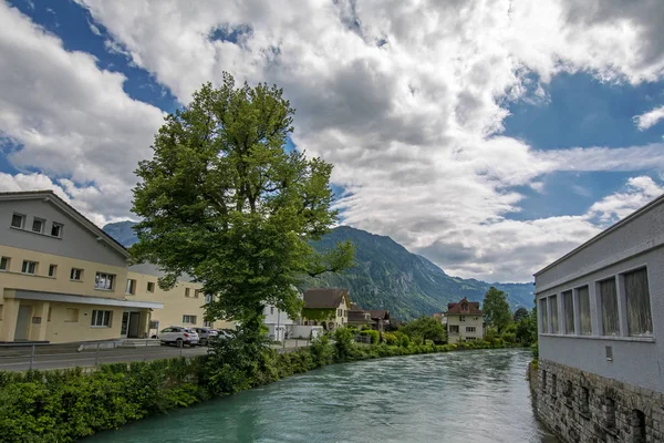 Wide angle perspective view of Aare River with turquoise water in Interlaken, Switzerland with Swiss Alps on background under the dramatic cloudy sky