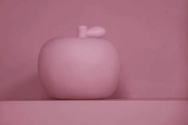 Pink abstract background with artificial apple on the shelf against the wall with soft shadow. Perfect background for text