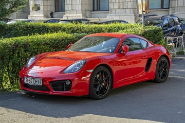 Bükreş, Romanya - 06 Ağustos 2019: Lüks kırmızı Porsche 718 Cayman S arka planda yeşil çalılarla sokağa park edildi