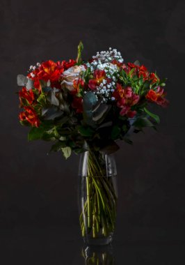 Soyut koyu gri arka planda cam vazoda çeşitli renkli çiçeklerden oluşan güzel bir buket. Çiçek açan bitkilerin eski tarz yaşamı