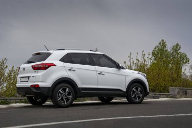 Erivan, Ermenistan - 16 Nisan 2020: Beyaz Kore kompakt Hyundai Creta (Hyundai ix25 olarak da bilinir) asfalt yola park edilmiş ve arka planda dramatik bulutlu gökyüzü altında yeşil ağaçlar var. Yan görünüm