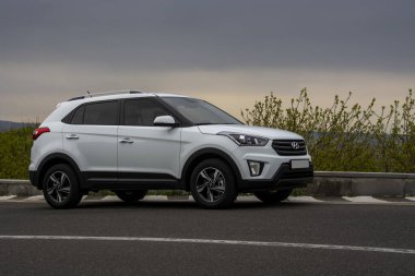 Erivan, Ermenistan - 16 Nisan 2020: Beyaz Kore kompakt Hyundai Creta (Hyundai ix25 olarak da bilinir) asfalt yola park edilmiş ve arka planda dramatik bulutlu gökyüzü altında yeşil ağaçlar var. Yan görünüm