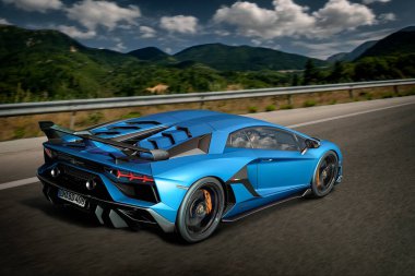Barselona, İspanya - 10 Temmuz 2019: Mavi Lamborghini Bulvarı SVJ V12 süper arabası, yeşil tepeler ve bulanık arkaplan ile otoyolda son sürat ilerliyor. Hareket bulanıklığı, dramatik gökyüzü