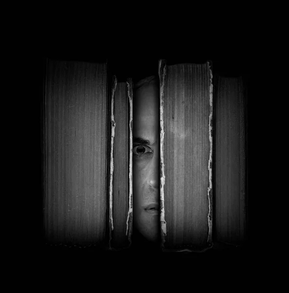 Surreal scene with close-up man's face with an amazed expression between old books on dark background. Bibliophile, education importance and imaginative literature concept. Black and white photography