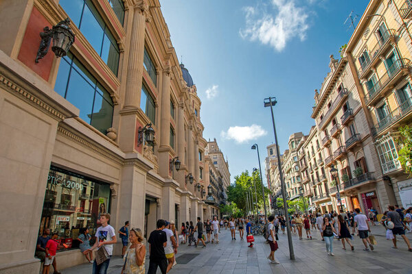 Barcelona, Spain - July 31, 2019: View of the historical buildings on the Avinguda del Portal de l Angel street in center of Barcelona in sunny day. People walk and shop. Low wide angle view