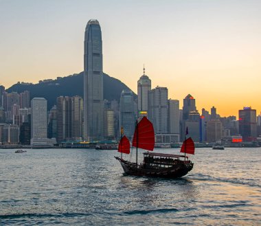 Hong Kong, Çin - 20 Şubat 2014: Victoria Limanı üzerindeki güzel gökdelenler, günbatımında kırmızı yelkenli hurda turist feribotu.