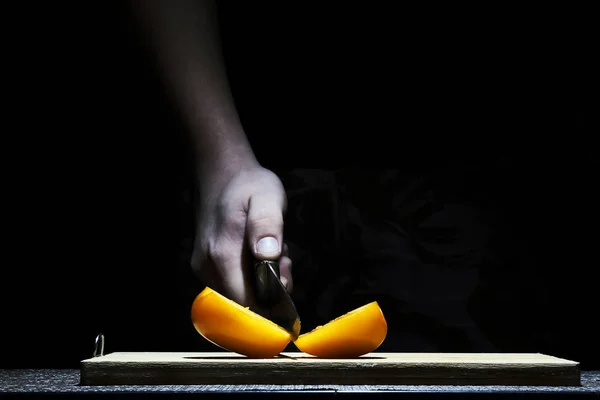 Chef na cozinha cortando um tomate com uma faca de cozinha afiada close-up em um fundo preto — Fotografia de Stock