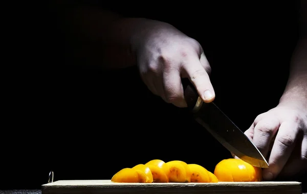 chef in the kitchen slicing a tomato with a sharp kitchen knife close-up on a black background