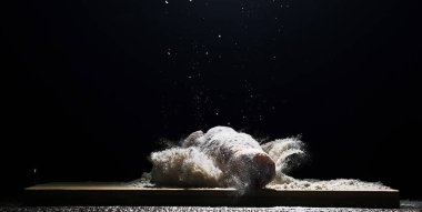 chicken, chicken drumstick in flour with flour dust flying in different directions on a black background