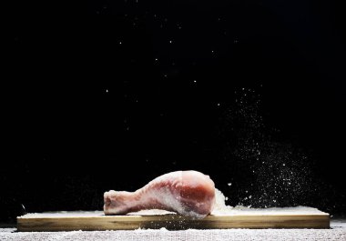 chicken, chicken drumstick in flour with flour dust flying in different directions on a black background