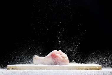 chicken, chicken drumstick in flour with flour dust flying in different directions on a black background