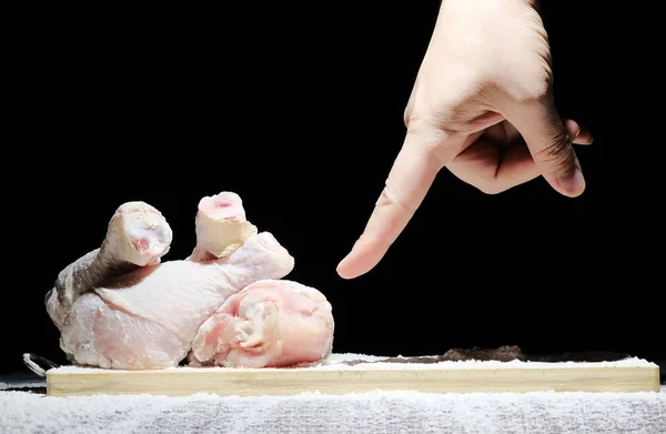 O chef na cozinha prepara frango, embrulhando a perna de frango em farinha. poeira, ação e movimentos na farinha. no fundo preto — Fotografia de Stock