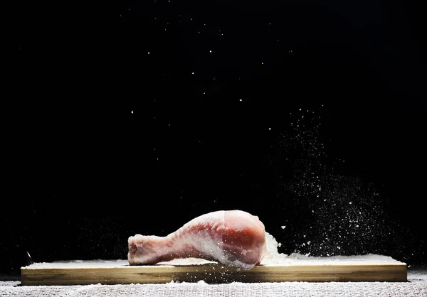 Chicken, chicken drumstick in flour with flour dust flying in different directions on a black background — Stock Photo, Image