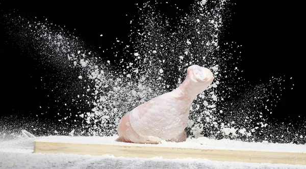 Frango, baqueta de frango na farinha com pó de farinha voando em direções diferentes em um fundo preto — Fotografia de Stock
