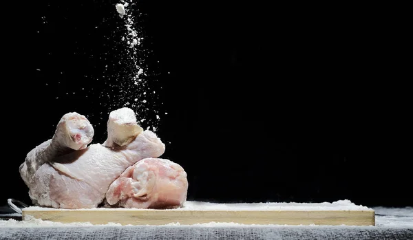Frango, baqueta de frango na farinha com pó de farinha voando em direções diferentes em um fundo preto — Fotografia de Stock