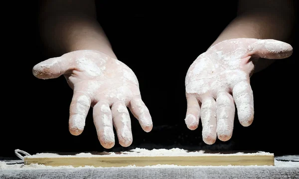 A chef with his hands in flour is preparing to cook a meal on a black background — Stock Photo, Image