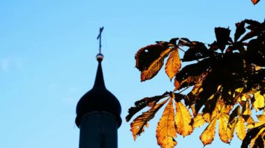 Kestane yapraklarının arasından mavi gökyüzünün arka planında bir kilise