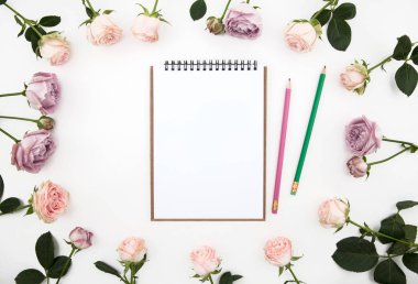 Defter kalemler etrafında pembe Gül çiçek ile. Masada beyaz arka plan üzerinde izole. Düz. Yukarıdan görünüm yatıyordu. Görünümü üst.