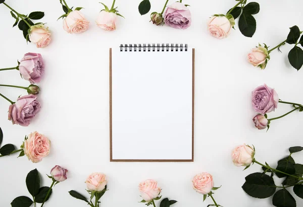 Temiz defter çiçekler üzerinde beyaz bir arka plan ile. Yukarıdan görüntüleyin. Düz yatıyordu. Görünümü üst.