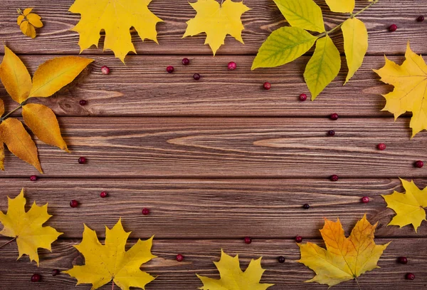 Renkli yaprakları ve ahşap kahverengi tahta üzerinde kırmızı meyveler ile sonbahar arka plan çerçeve.