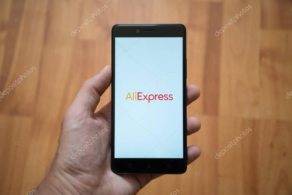 London, United Kingdom, june 5, 2017: Man holding smartphone with Aliexpress logo on the screen. Laminate wood background.
