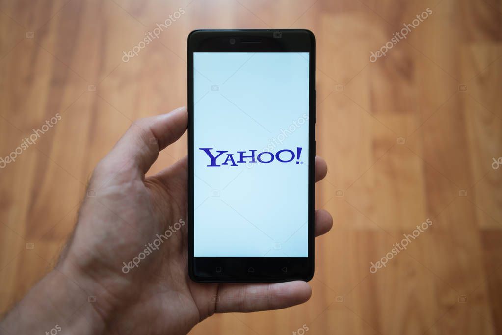 London, United Kingdom, june 5, 2017: Man holding smartphone with Yahoo logo on the screen. Laminate wood background.