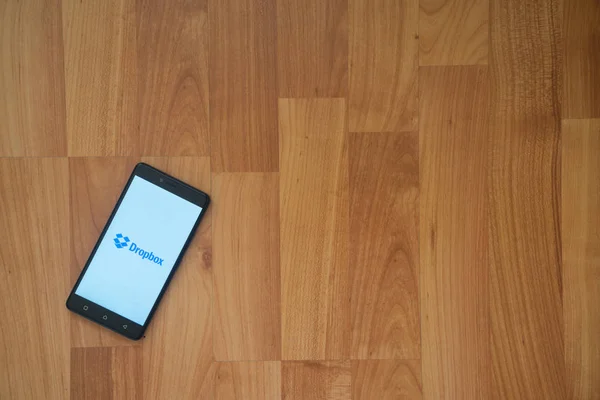 Na obrazovku smartphonu na dřevěné pozadí logo Dropbox. — Stock fotografie