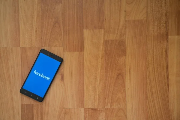 Facebook logo na obrazovku smartphonu na dřevěné pozadí. — Stock fotografie