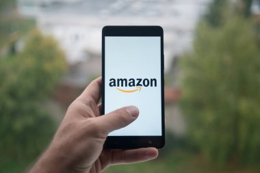 Üstünde belgili tanımlık perde smartphone parmak ile Amazon logolu tutan adam.