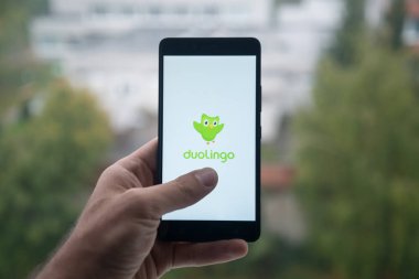 Üstünde belgili tanımlık perde smartphone ile parmak Duolingo logolu tutan adam.