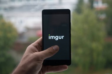 Üstünde belgili tanımlık perde smartphone parmaklı Imgur logolu tutan adam.