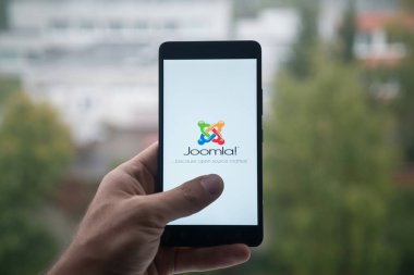 Üstünde belgili tanımlık perde smartphone parmak ile Joomla logolu tutan adam.