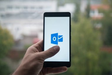 Üstünde belgili tanımlık perde smartphone ile Microsoft Office outlook logosu ile parmak tutan adam.