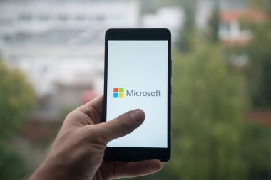 Üstünde belgili tanımlık perde smartphone parmak ile Microsoft logolu tutan adam.