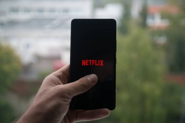 Üstünde belgili tanımlık perde smartphone parmak ile Netflix logolu tutan adam.