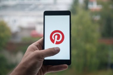 Üstünde belgili tanımlık perde smartphone ile parmak Pinterest logolu tutan adam.