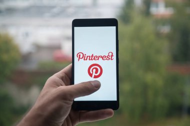 Üstünde belgili tanımlık perde smartphone ile parmak Pinterest logolu tutan adam.