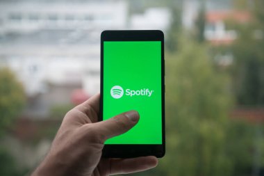 Üstünde belgili tanımlık perde smartphone parmak ile Spotify logolu tutan adam.
