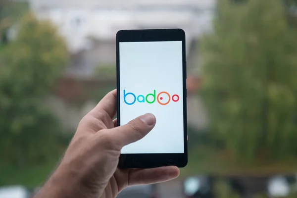 Człowiek posiadający smartfon z Badoo logo z palca na ekranie. — Zdjęcie stockowe