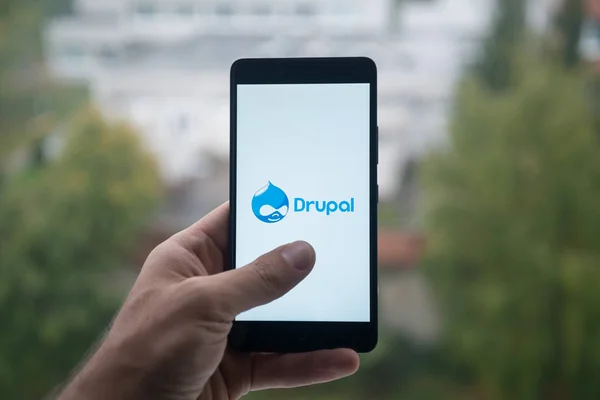Man met smartphone met Drupal logo met de vinger op het scherm. — Stockfoto
