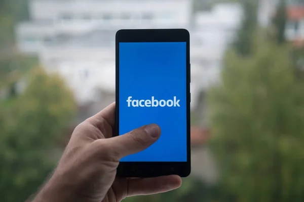 Мужчина держит смартфон с логотипом Facebook с пальцем на экране . — стоковое фото