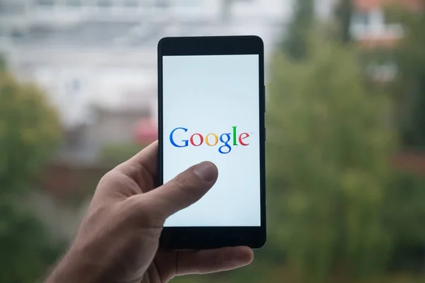 Hombre sosteniendo el teléfono inteligente con el logotipo de Google con el dedo en la pantalla . — Foto de Stock