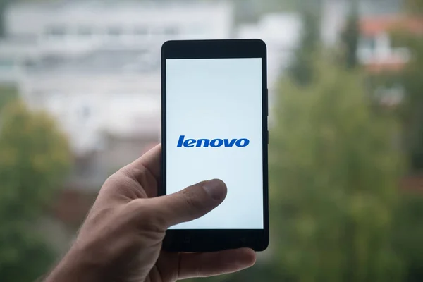 Homme tenant smartphone avec logo Lenovo avec le doigt sur l'écran . — Photo