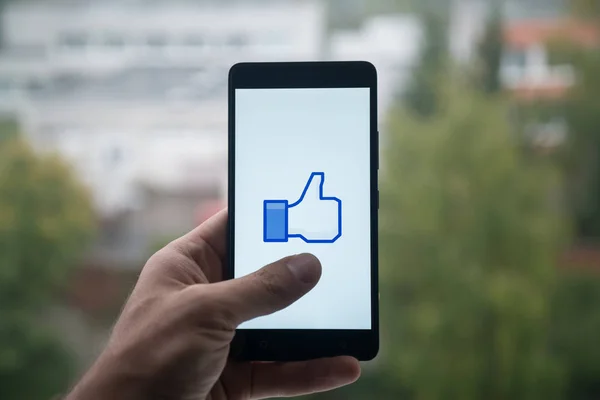 Мужчина, держащий смартфон с логотипом Facebook с пальцем на экране . — стоковое фото