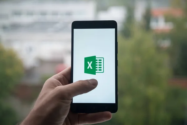 Człowiek gospodarstwa smartphone z programu Microsoft office excel logo z palca na ekranie. — Zdjęcie stockowe