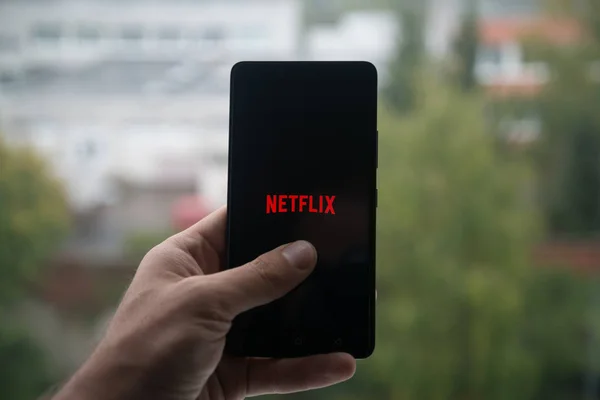 Homem segurando smartphone com logotipo Netflix com o dedo na tela . — Fotografia de Stock